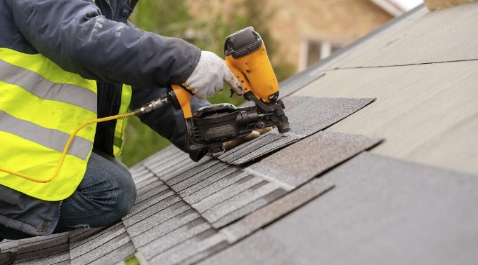 roofer using nail gun to install shingles